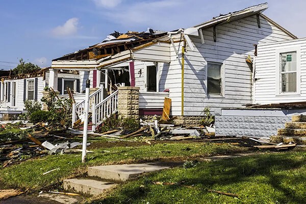 An emergency restoration team assesses a damaged home with a partially collapsed roof and debris scattered around following a severe storm, showcasing the destructive power of natural disasters.